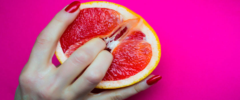 Dedos de mujer apretando una naranja roja