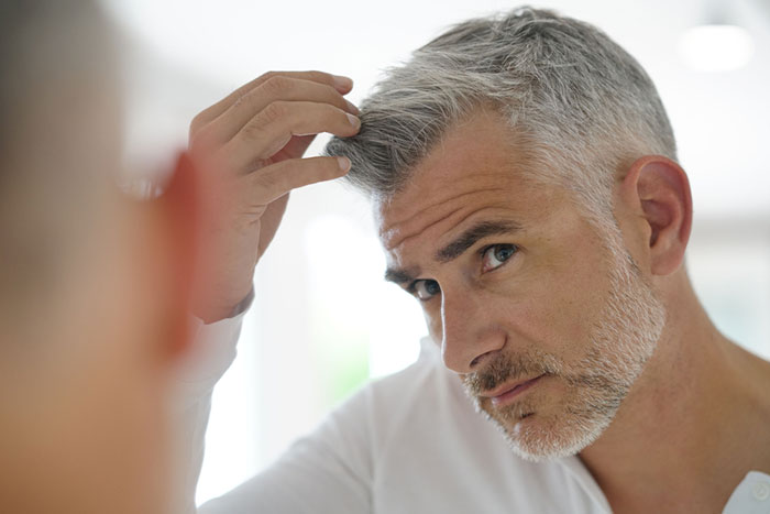 Hombre de mediana edad, con el pelo blanco y mirándose al espejo.